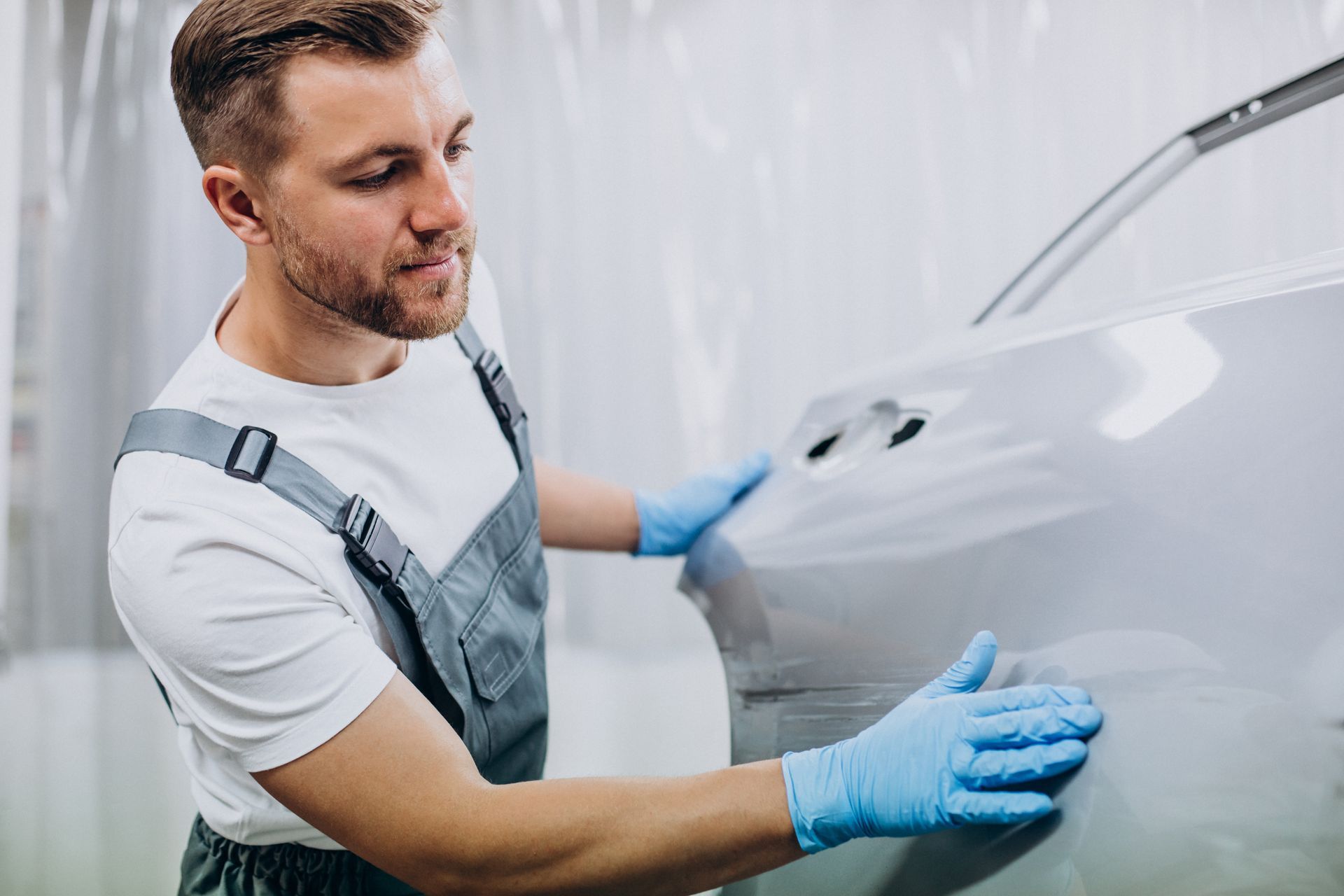 A man is spray painting a red car in a paint booth.