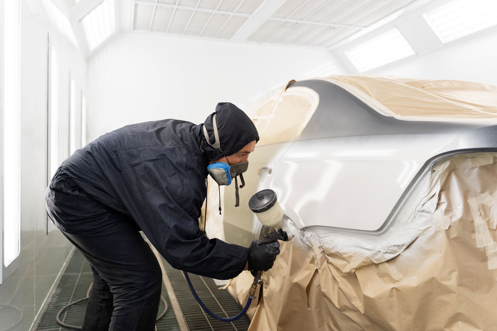 Person in protective gear sprays paint on car body in a paint booth.