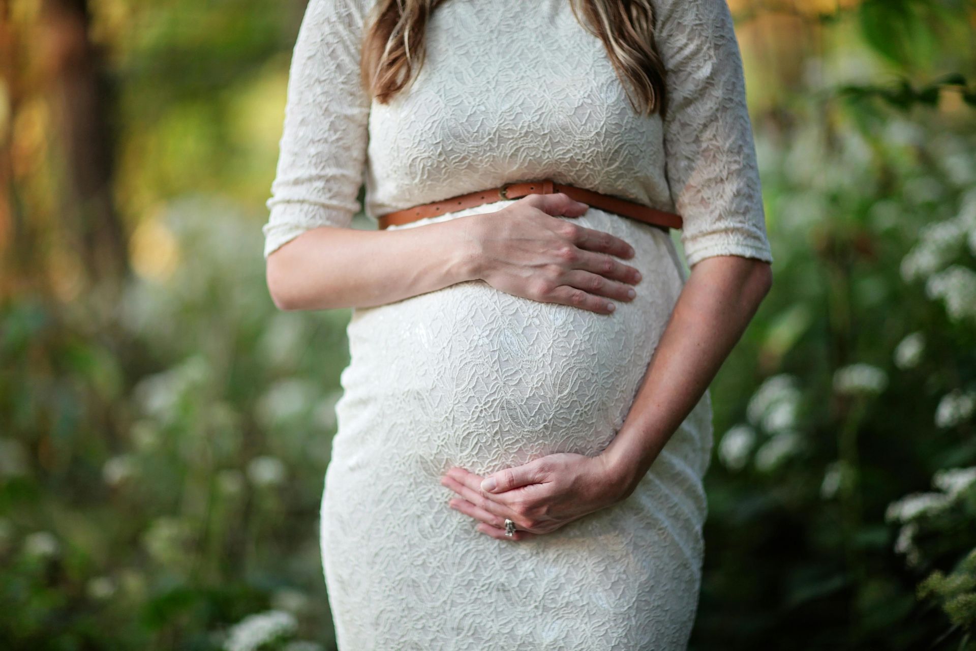 Eine schwangere Frau in einem weißen Kleid hält ihren Bauch.