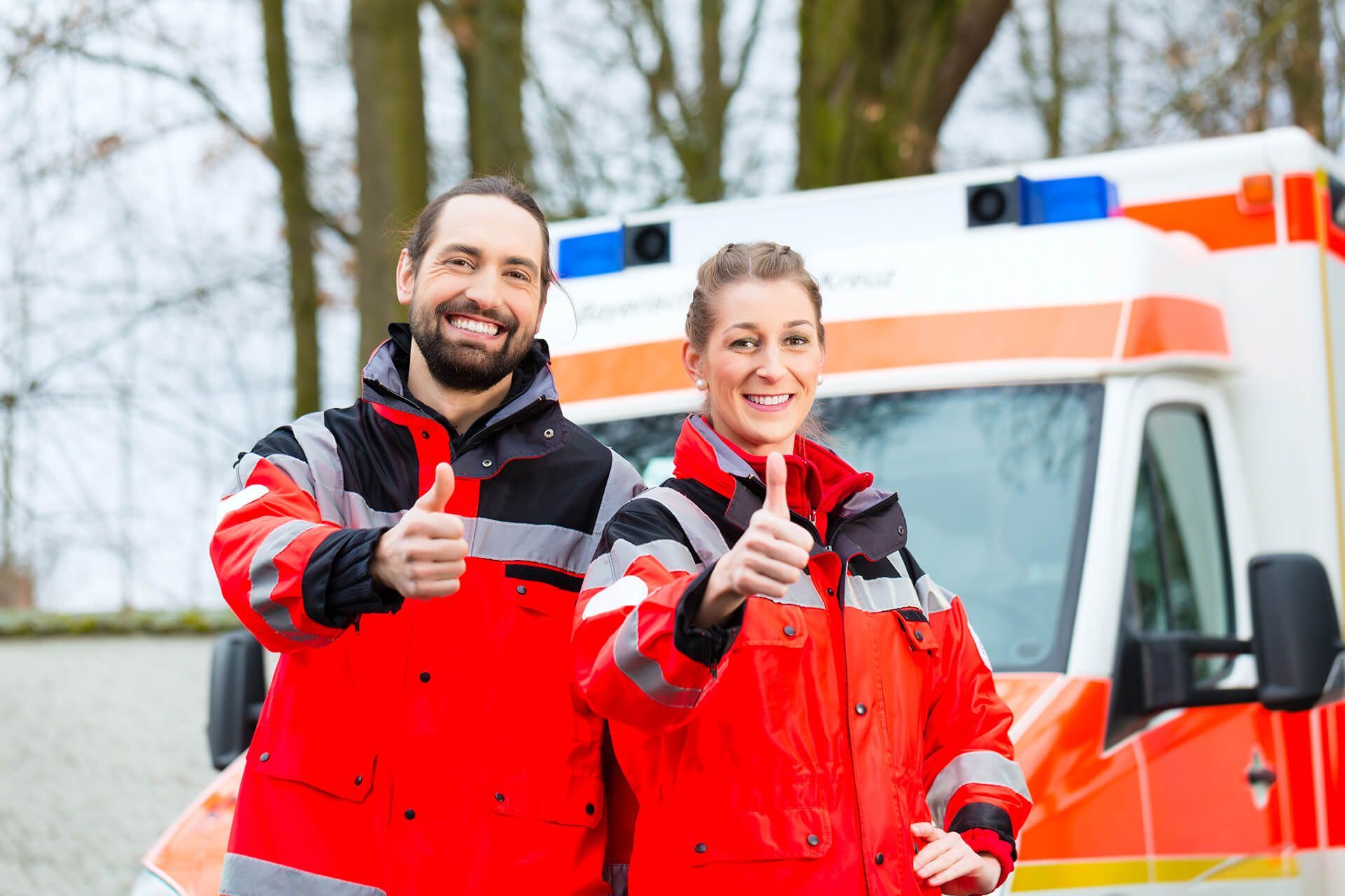 A man and a woman giving a thumbs up in front of an ambulance