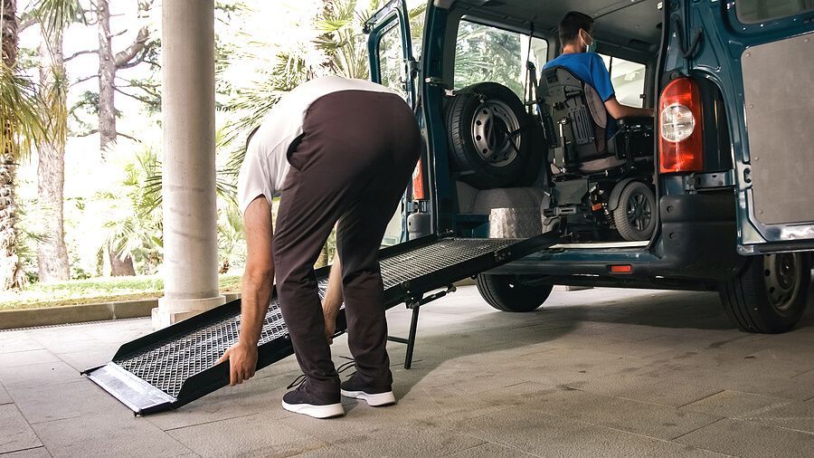 A man is loading a wheelchair into a van with a ramp.