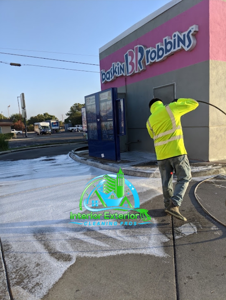 A man in a yellow jacket is cleaning the sidewalk in front of a building that says bakkin robbins