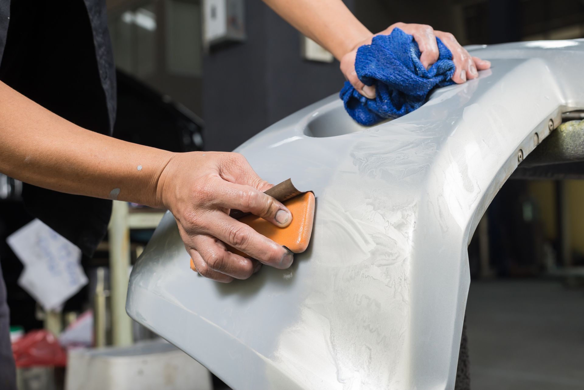 A person is sanding a car bumper with a sander.