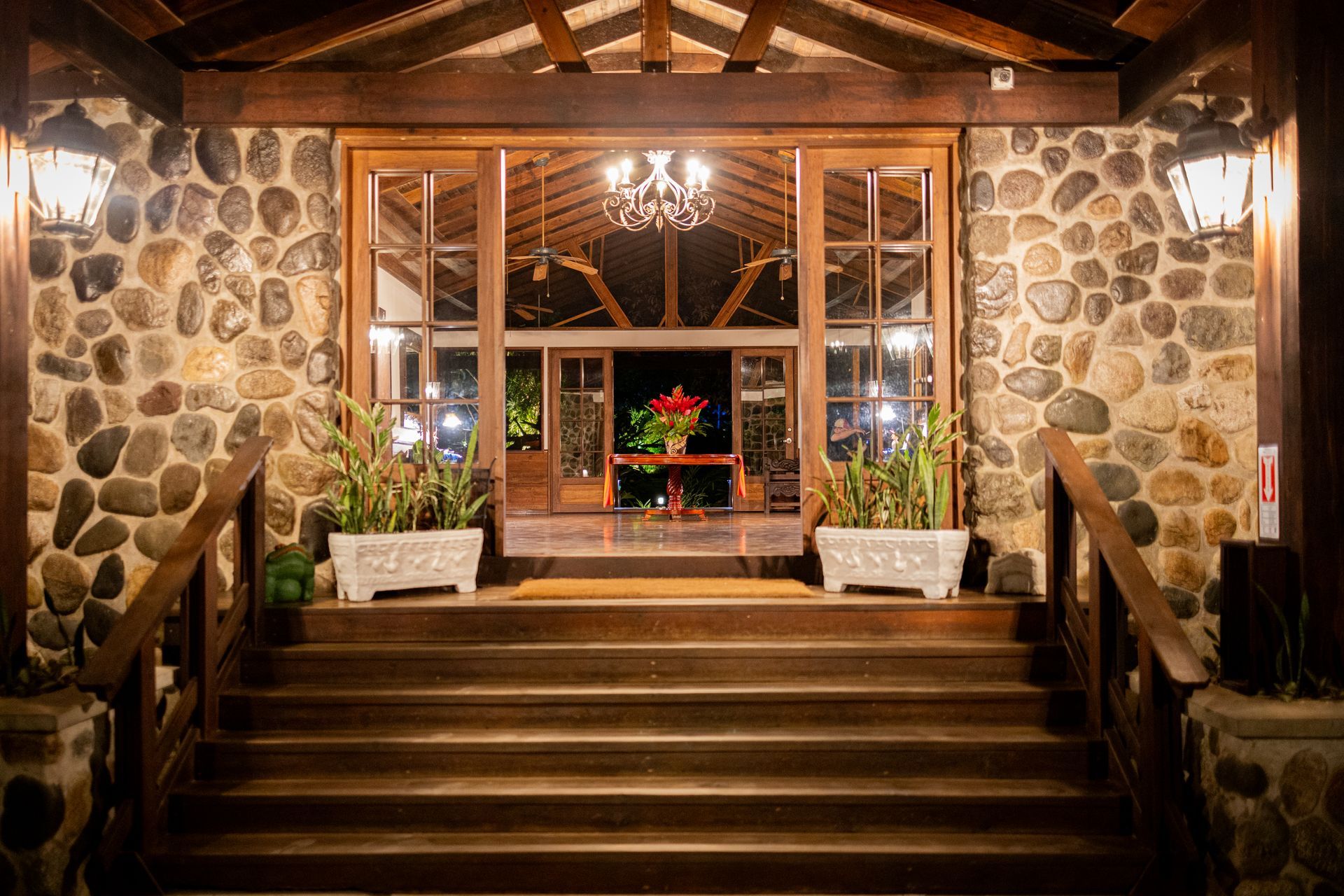 The entrance to a stone building with wooden stairs and a chandelier.