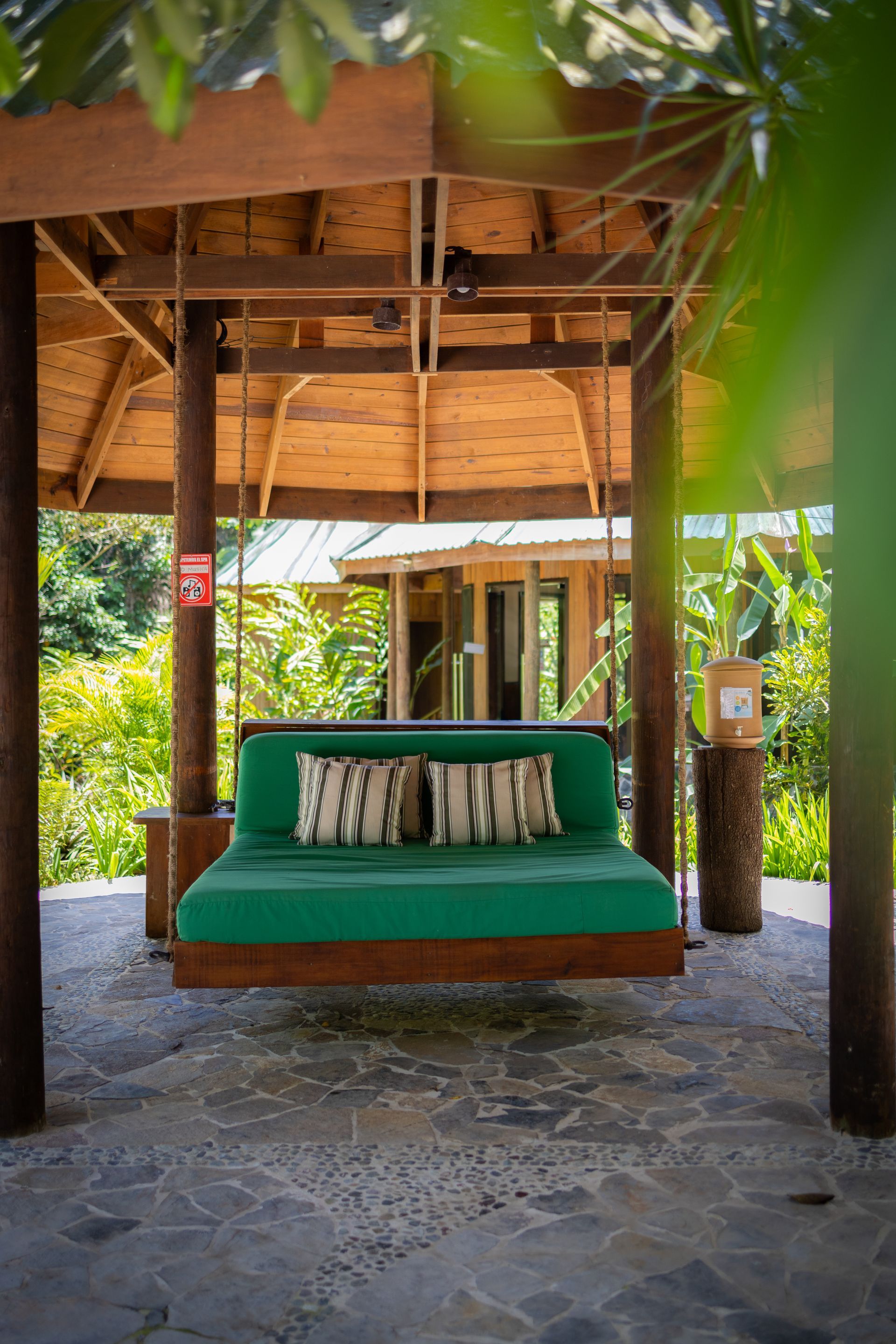 A green couch is hanging from the ceiling of a gazebo.