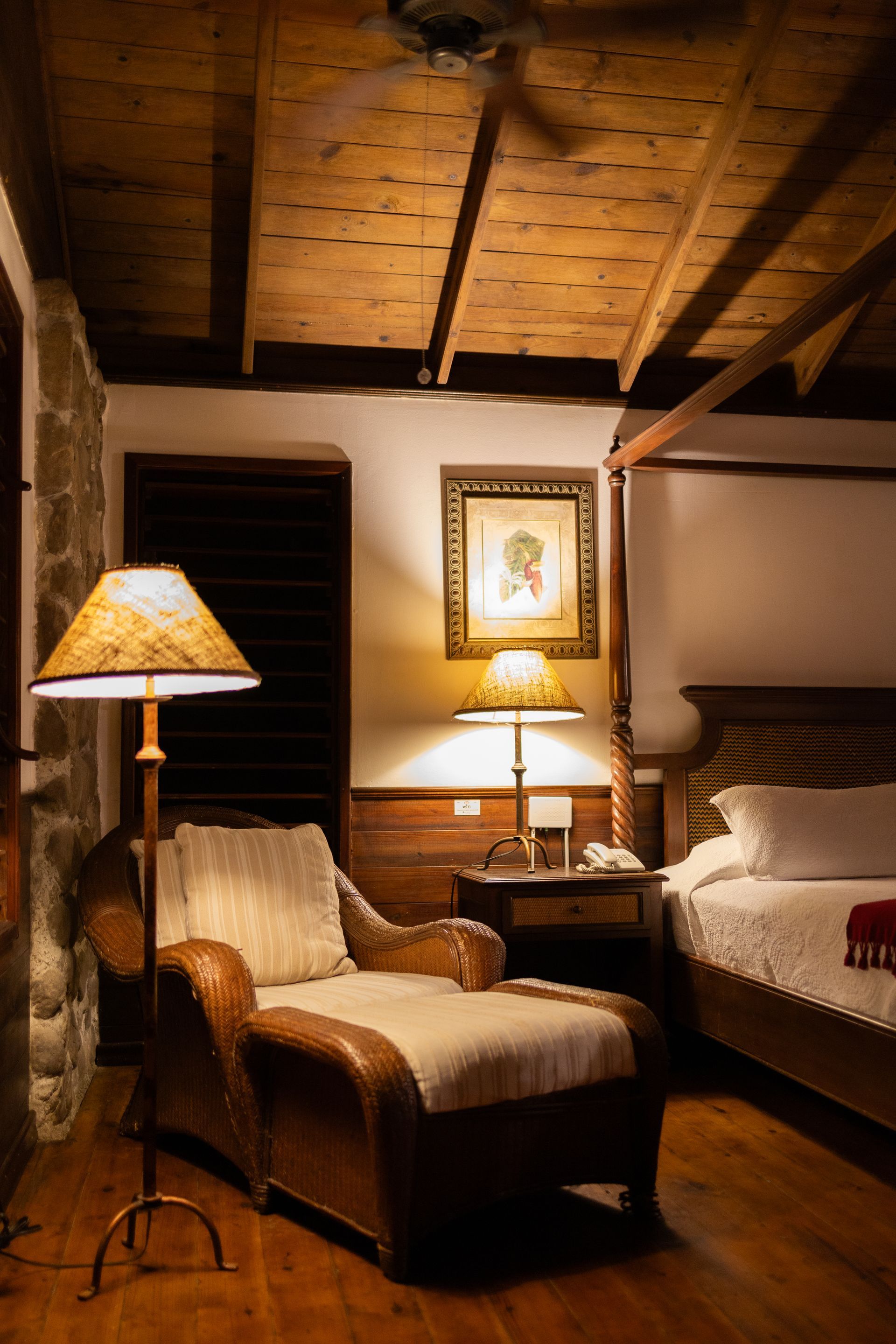 A bedroom with a canopy bed , chair , lamp and ottoman.