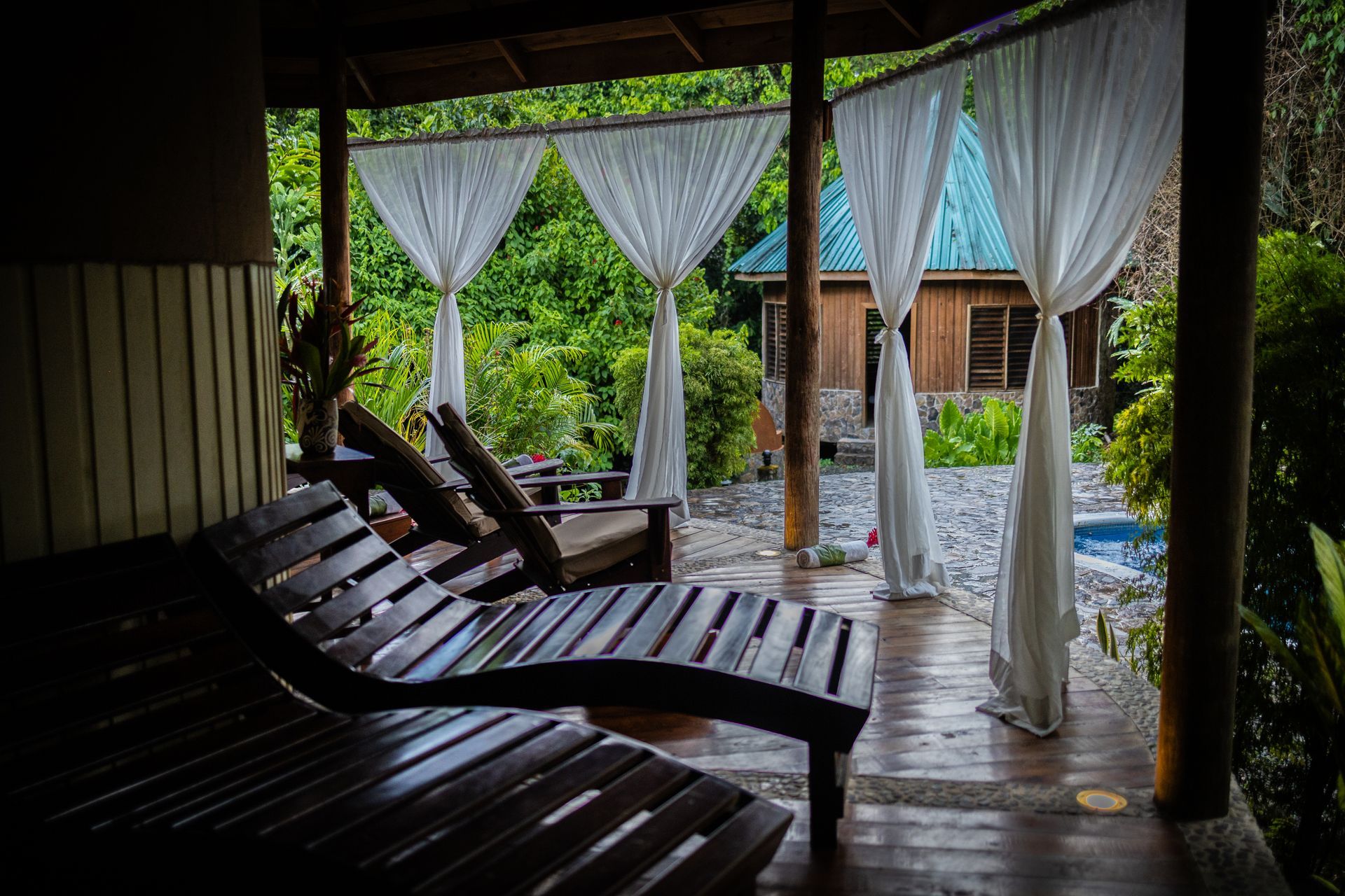 A patio with wooden chairs and white curtains.