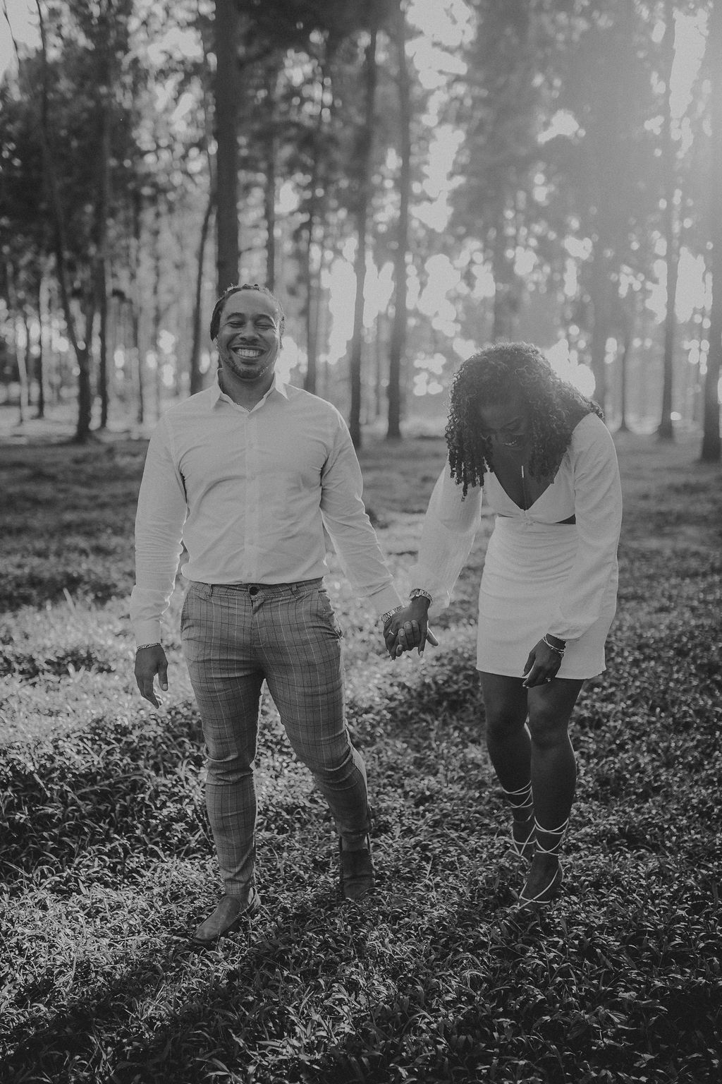 A black and white photo of a man and woman holding hands in the woods.