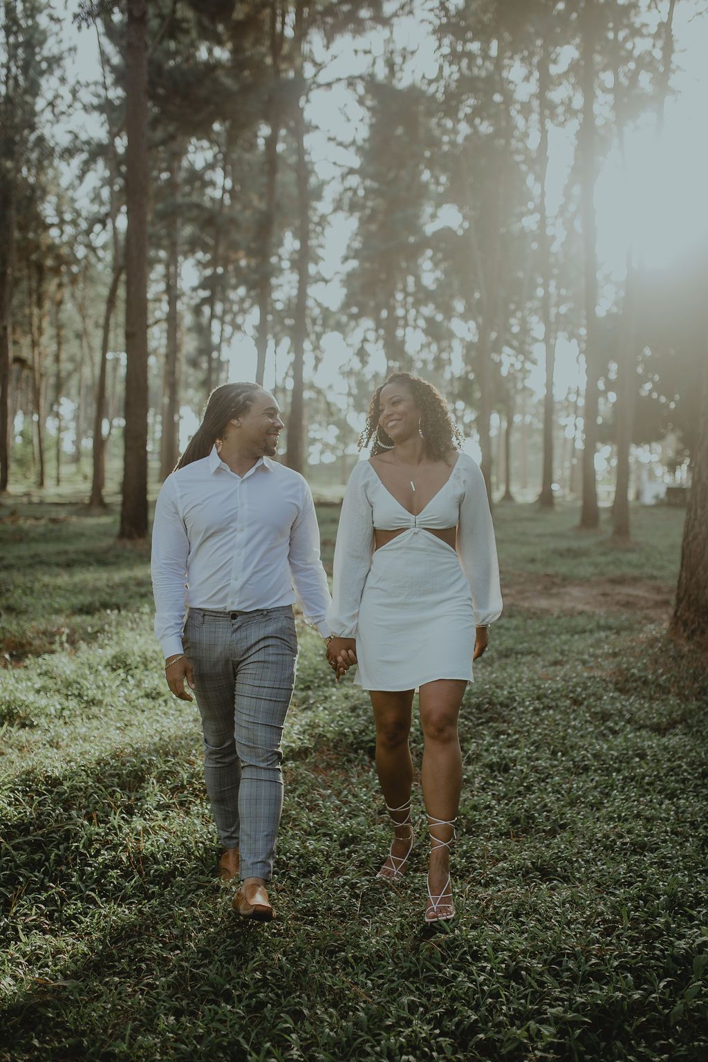 A man and a woman are walking through a forest holding hands.