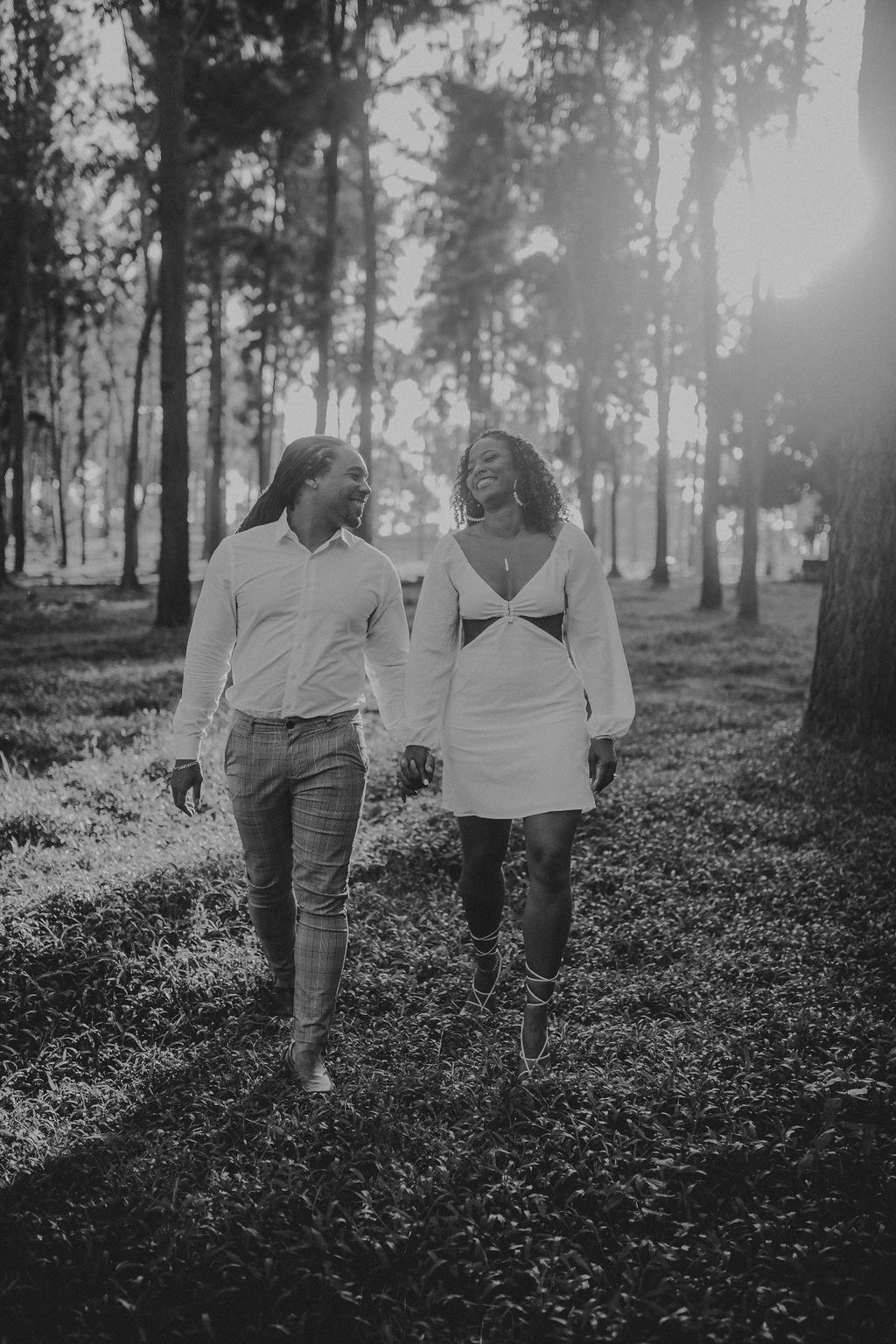A man and a woman are walking through a forest holding hands.