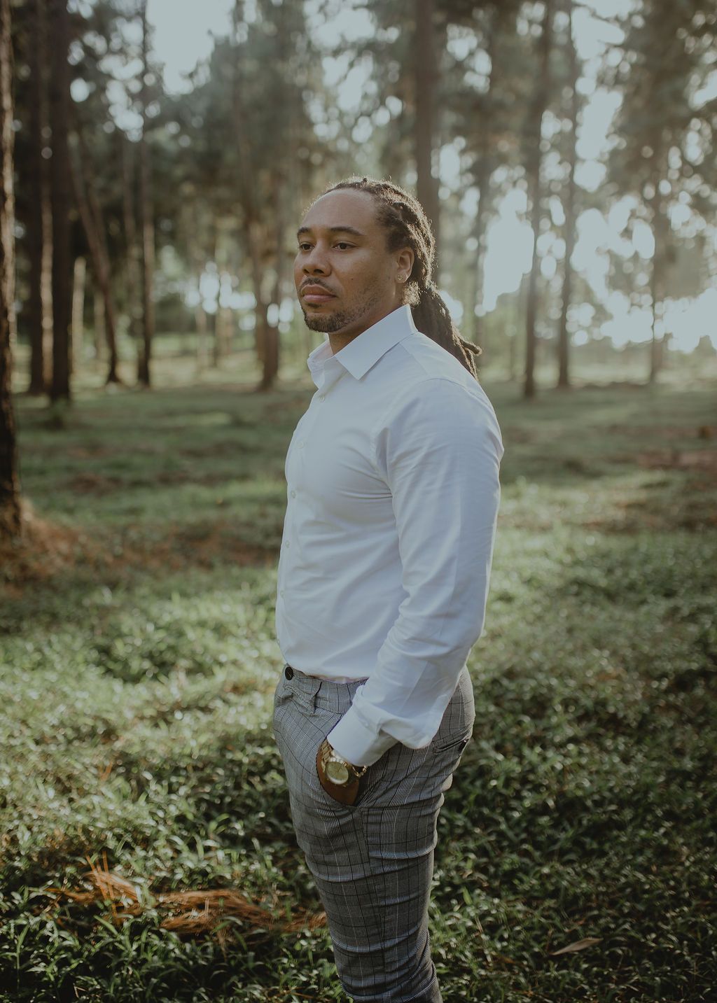 A man in a white shirt and plaid pants is standing in a field.