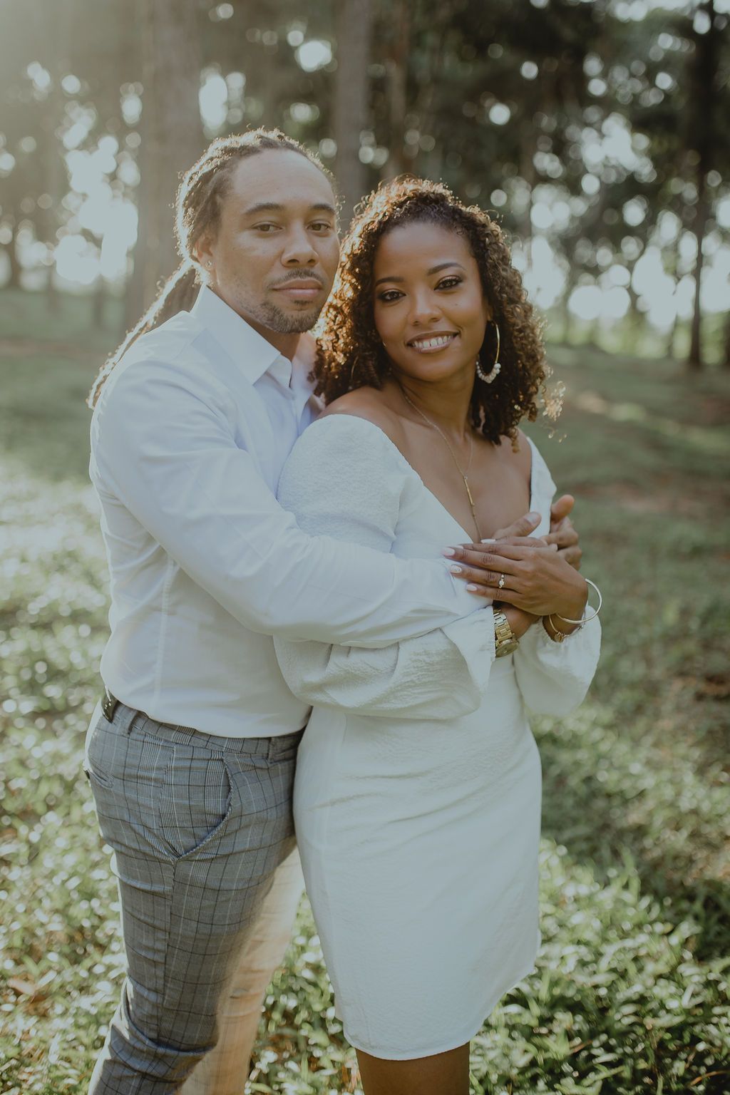 A man and a woman are posing for a picture in a field . the woman is wearing a white dress.