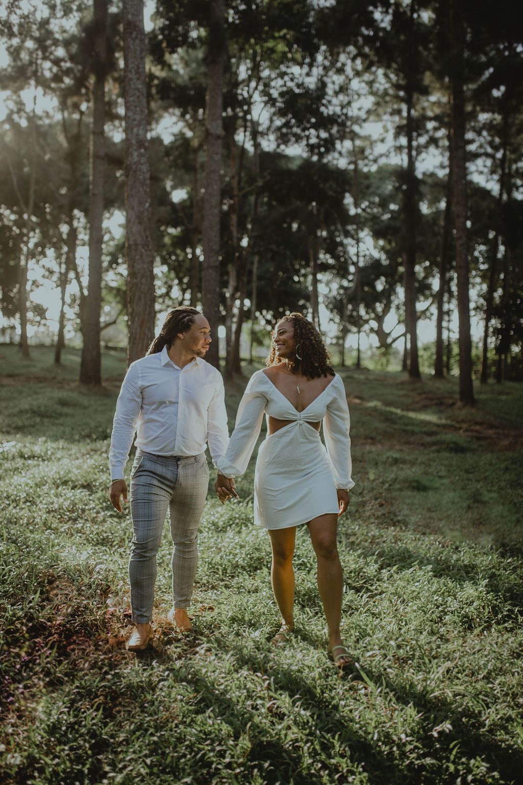 A man and a woman are walking through a field holding hands.