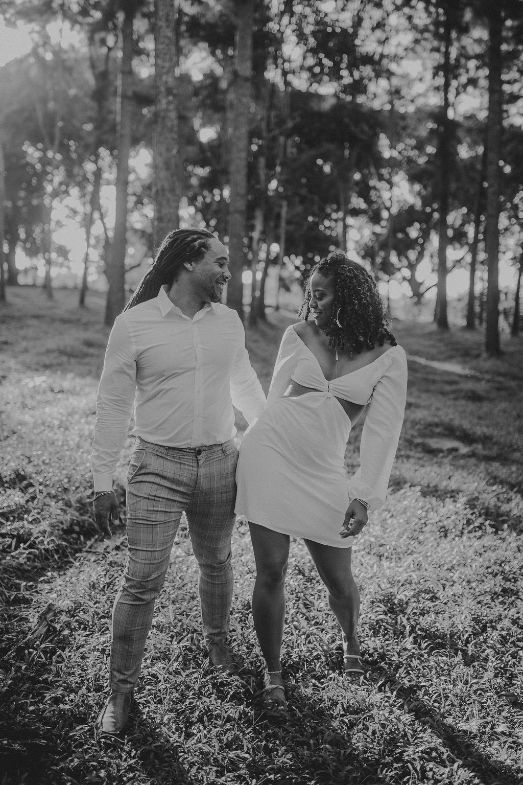 A black and white photo of a man and woman holding hands in the woods.
