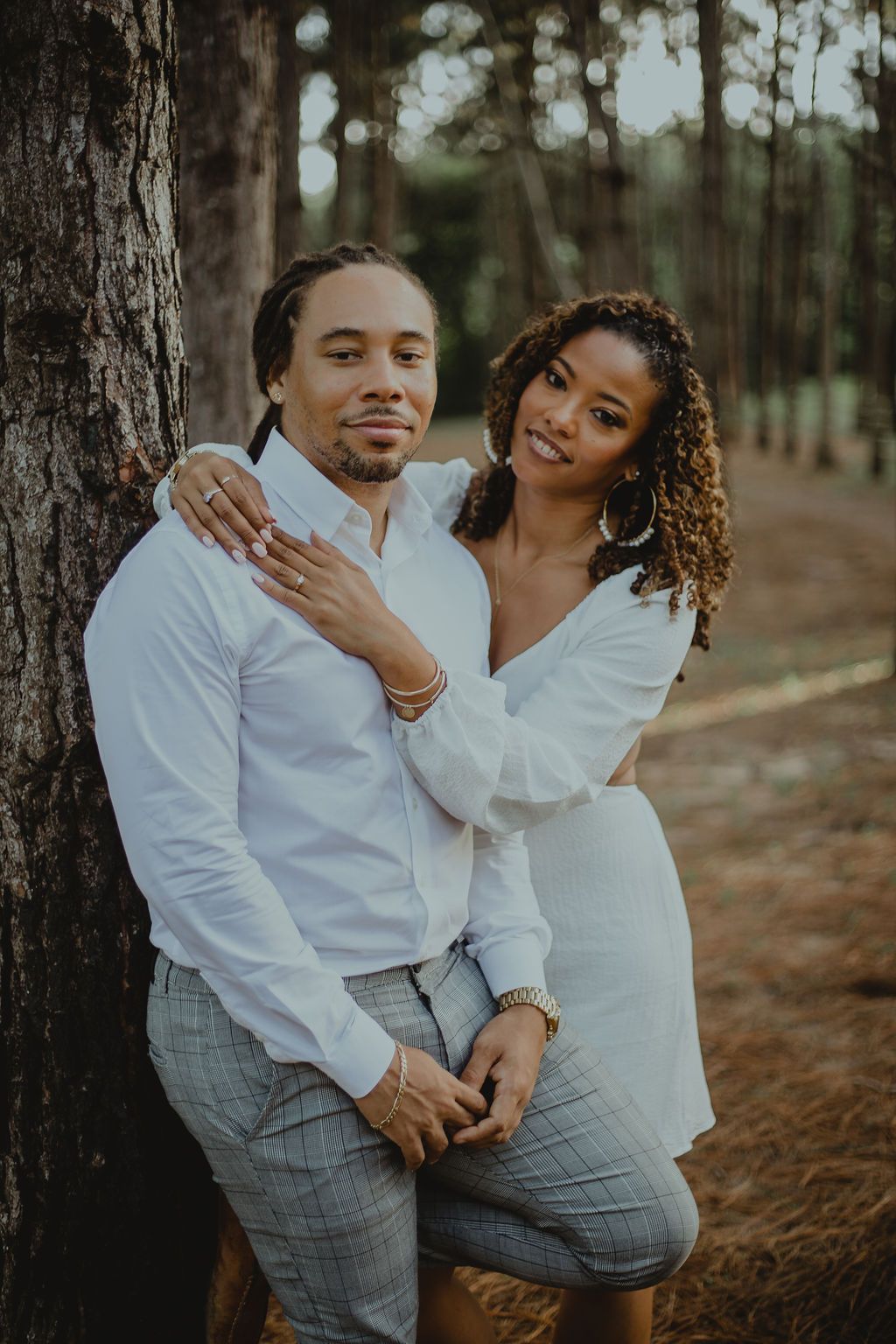 A man and a woman are sitting next to a tree in the woods.