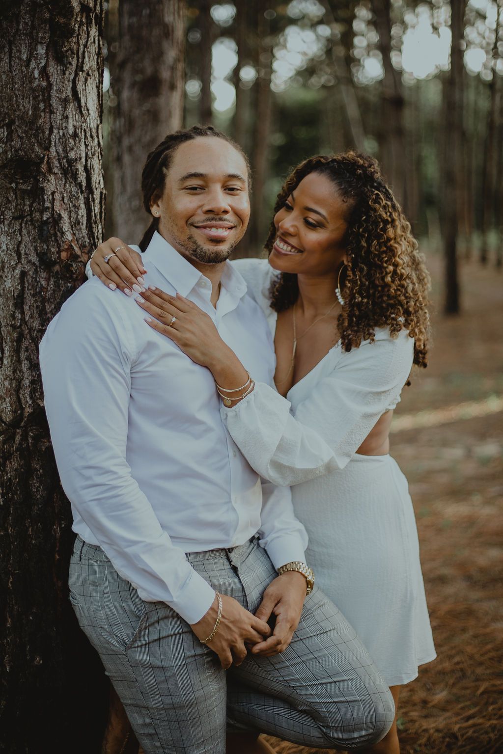 A man and a woman are leaning against a tree in the woods.