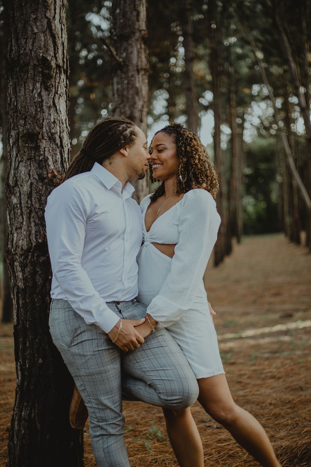 A man and a woman are leaning against a tree in the woods.