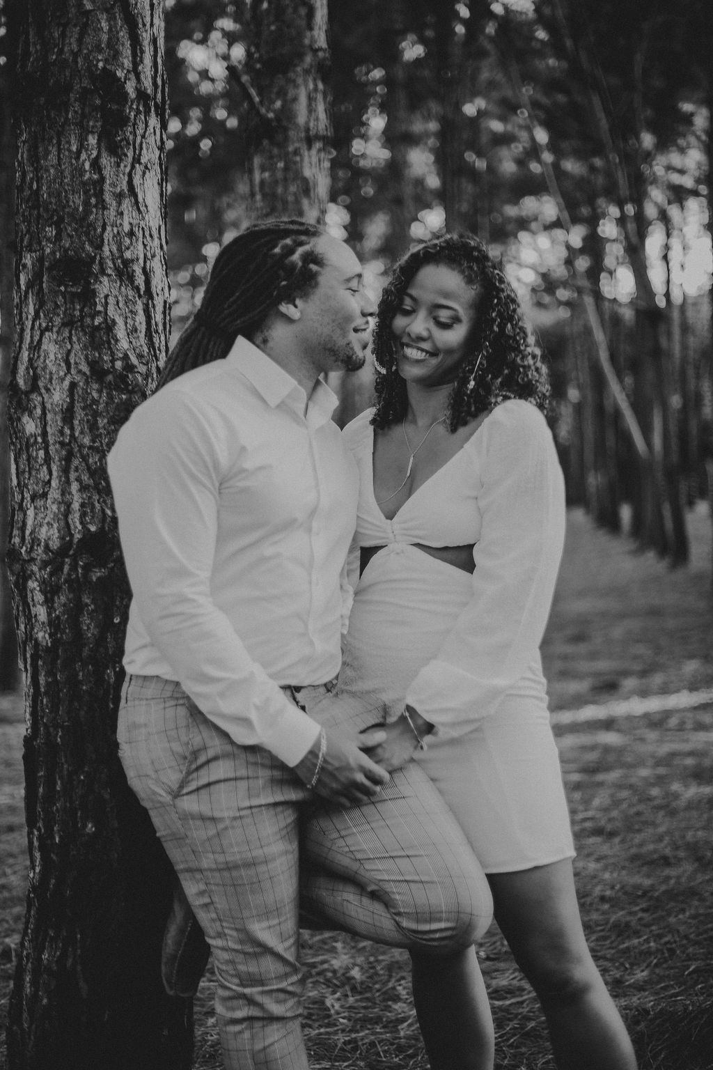 A black and white photo of a man and woman standing next to a tree.