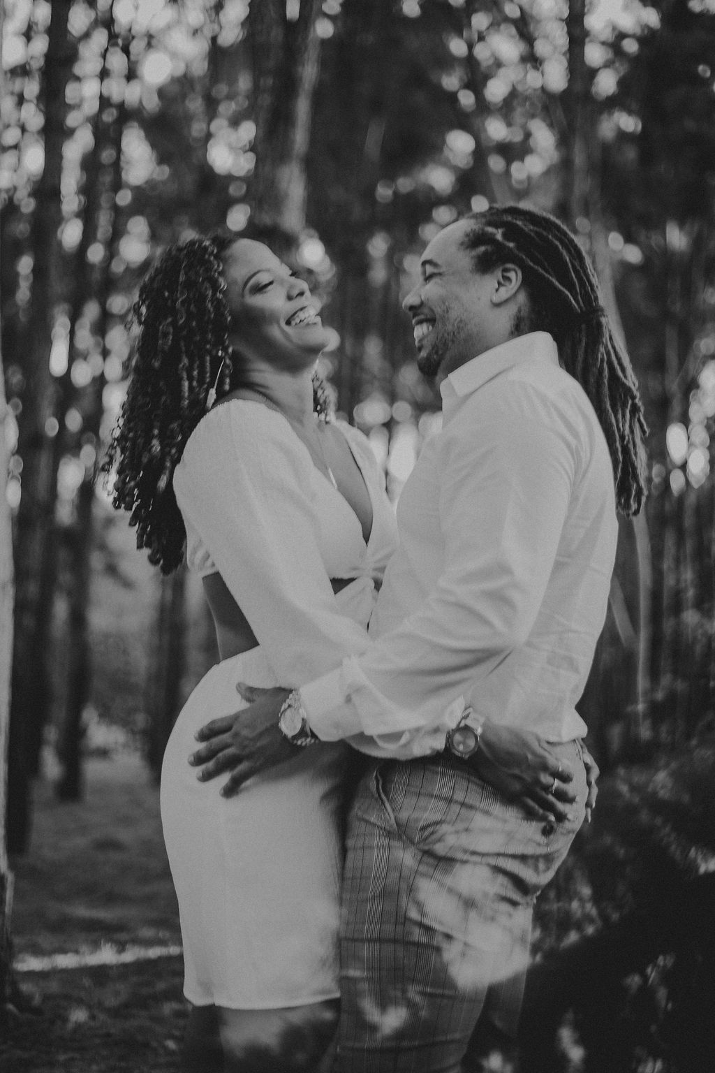 A black and white photo of a man and woman hugging each other in the woods.