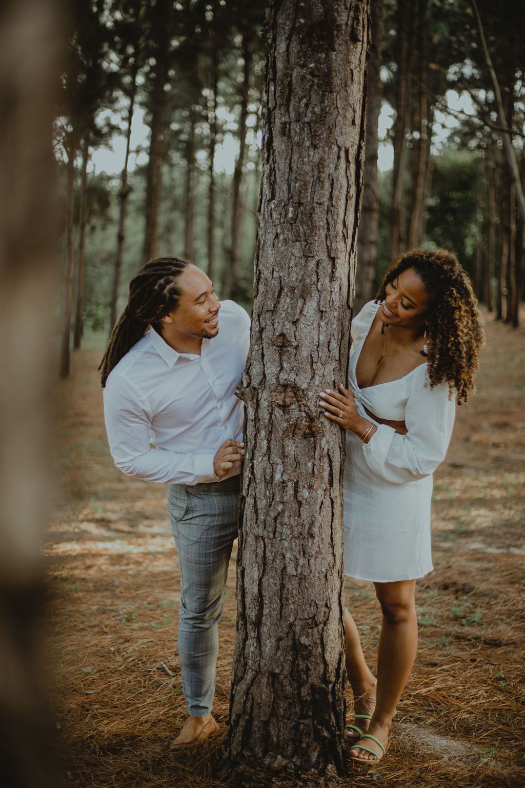 A man and a woman are hugging a tree in the woods.