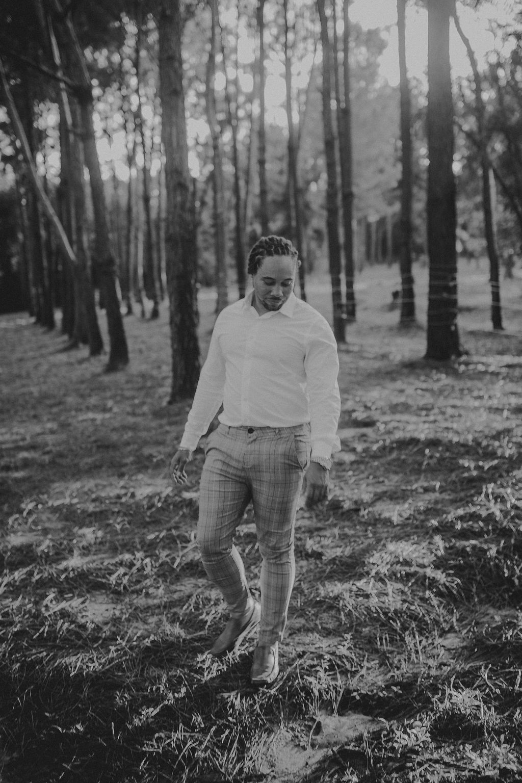 A black and white photo of a man walking through a forest.