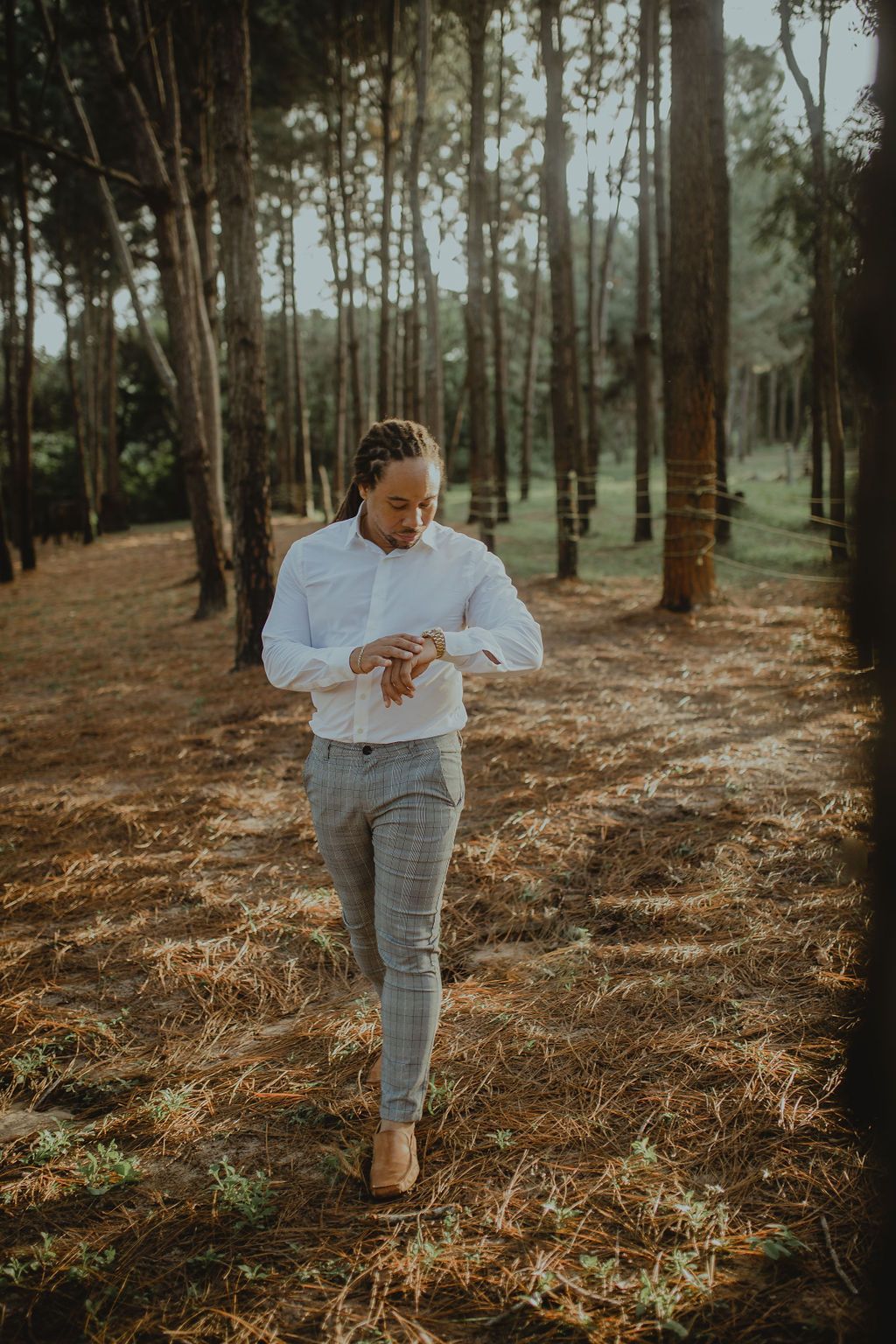 A man is walking through a forest looking at his watch.