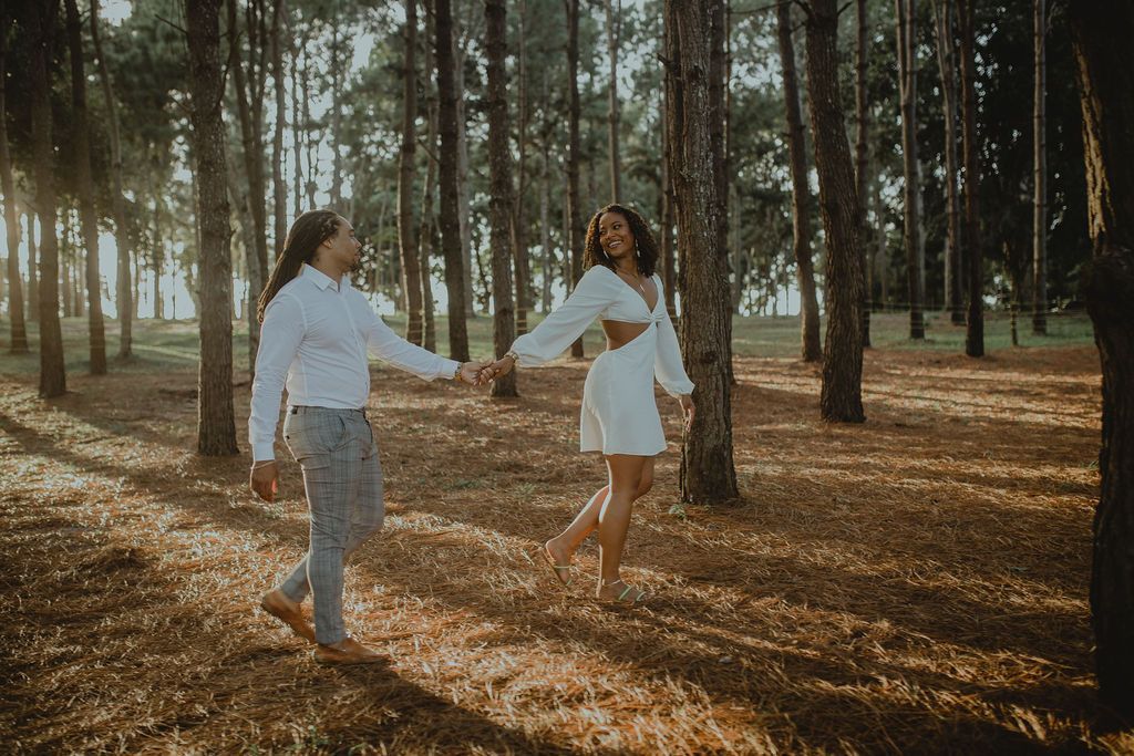 A man and a woman are walking through a forest holding hands.