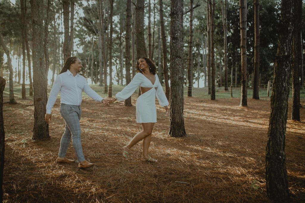 A man and a woman are walking through a forest holding hands.