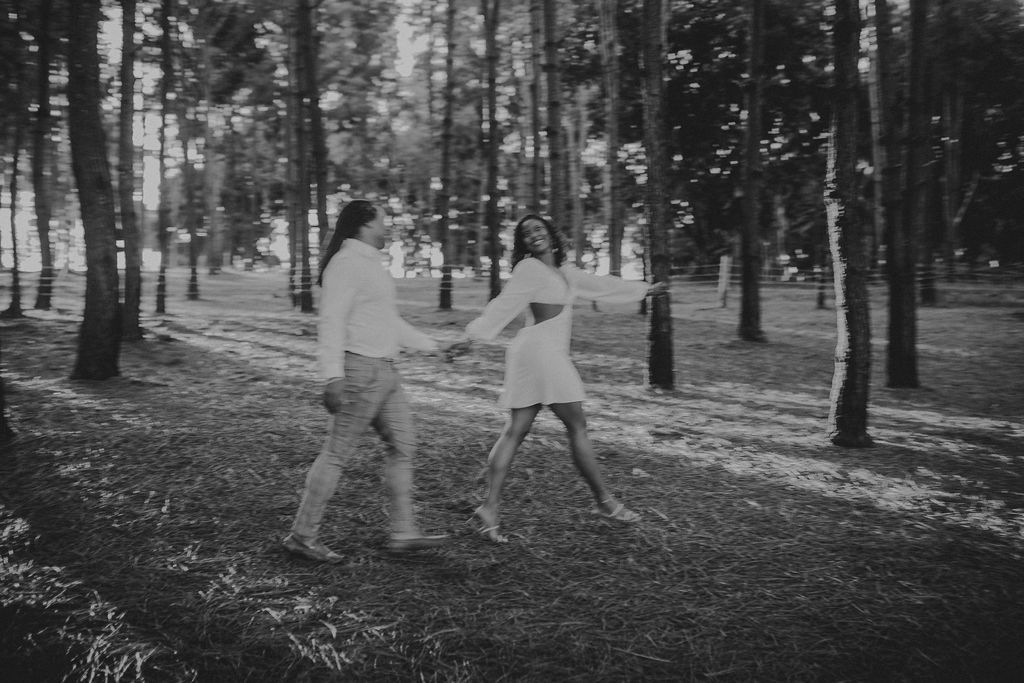 A black and white photo of a man and woman holding hands in the woods.
