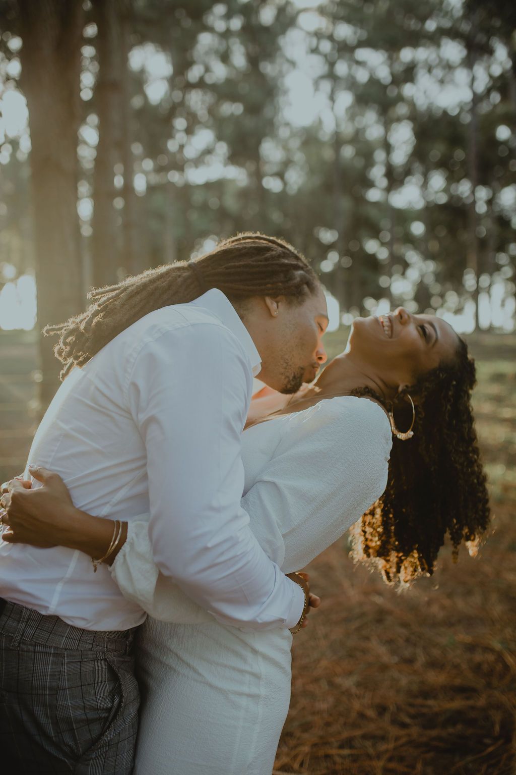 A man is holding a woman in his arms and kissing her in the woods.