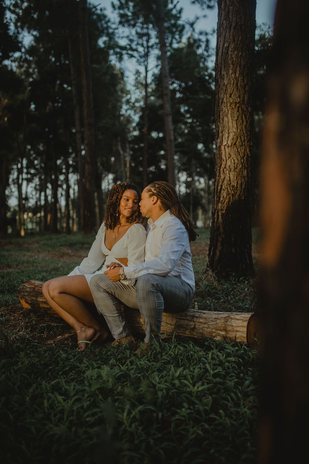A man and a woman are sitting on a log in the woods.