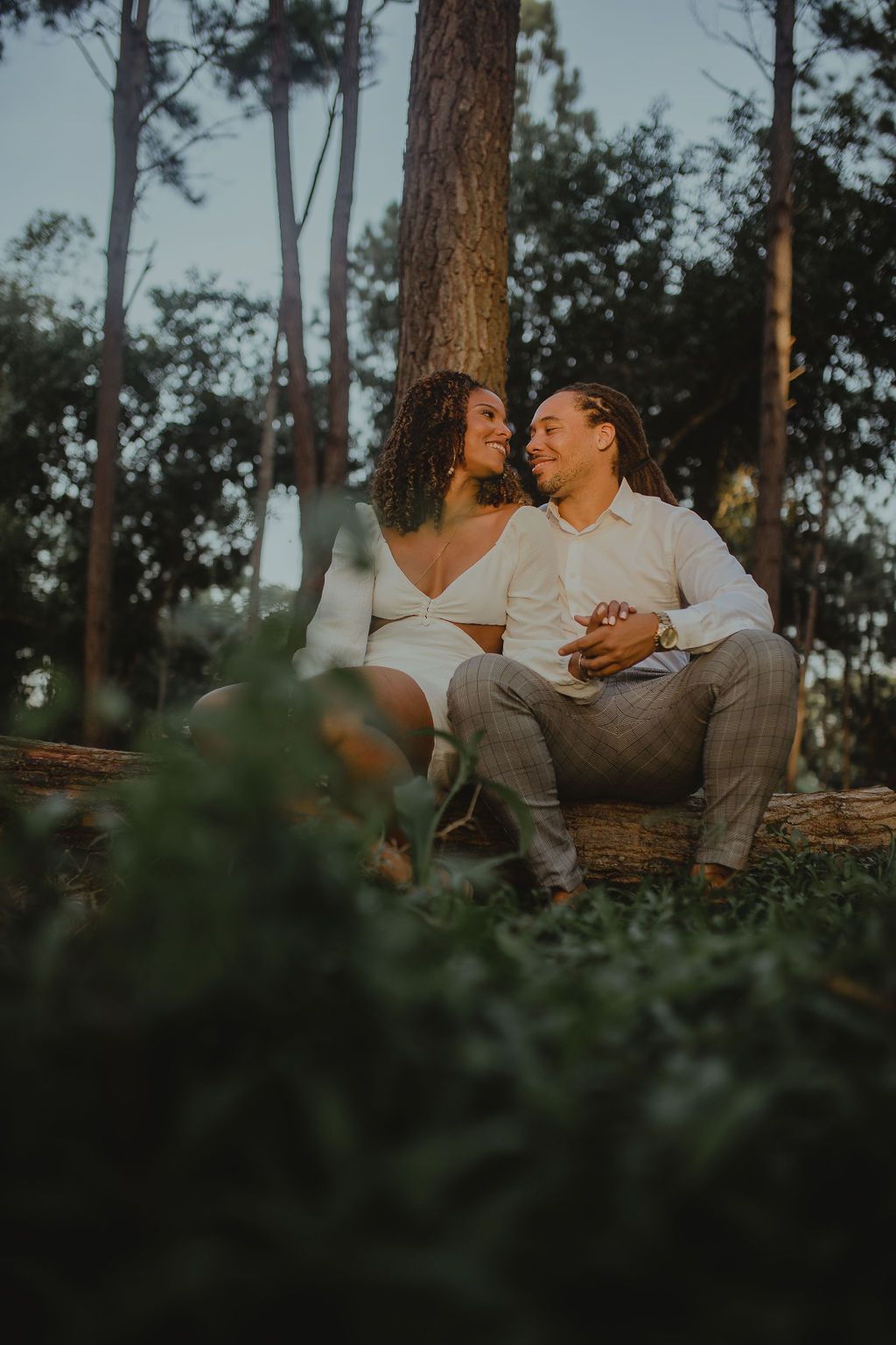 A man and a woman are sitting on a log in the woods.