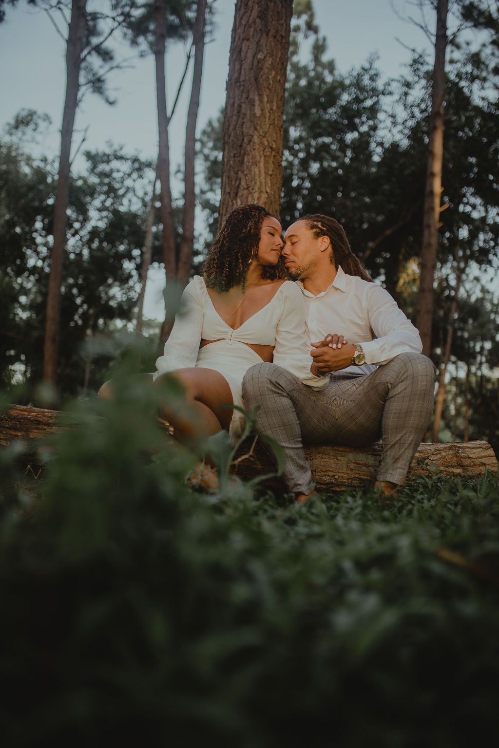 A man and a woman are sitting on a log in the woods.