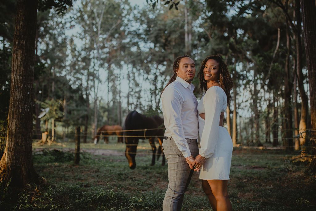 A man and a woman are holding hands in front of a horse in a field.