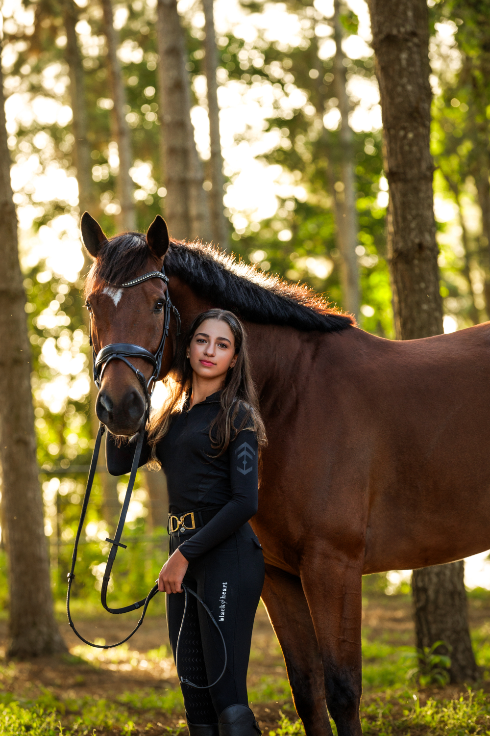 A woman is standing next to a brown horse in the woods.