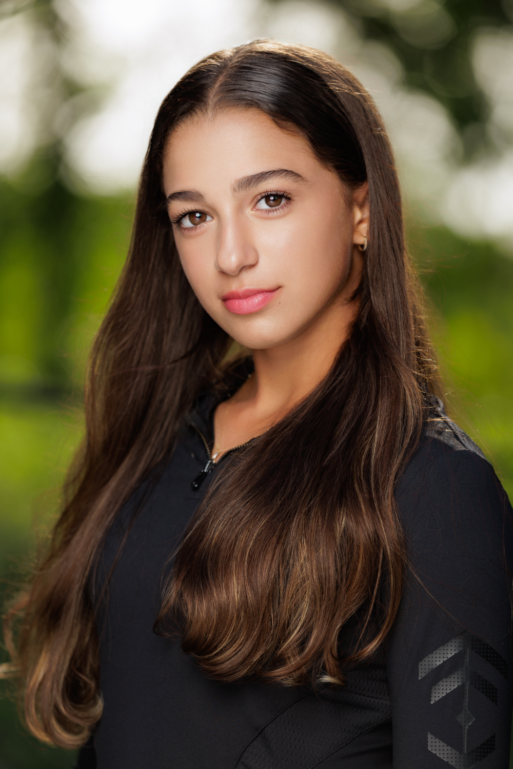 A young woman with long brown hair is wearing a black shirt and looking at the camera.