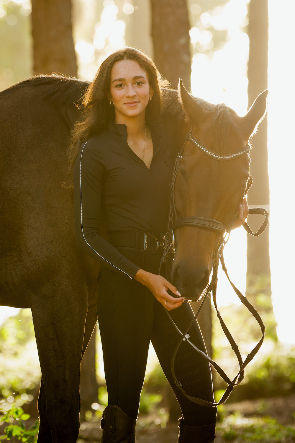 A woman is standing next to a brown horse in the woods.
