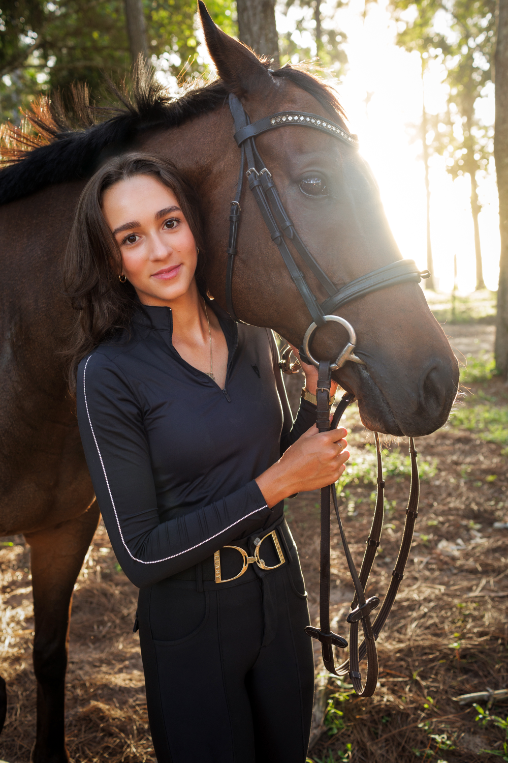 A woman is standing next to a brown horse in the woods.