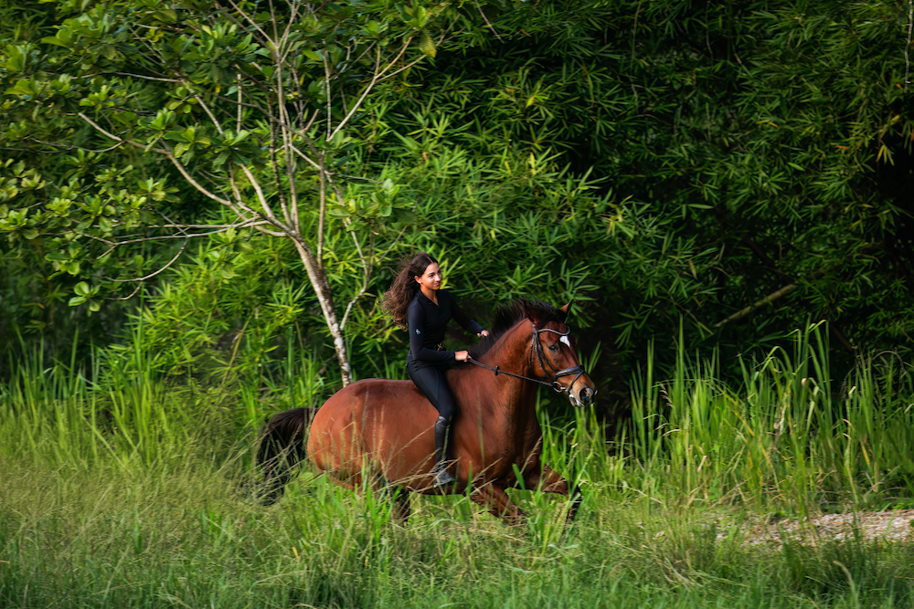 A woman is riding a brown horse through a grassy field.