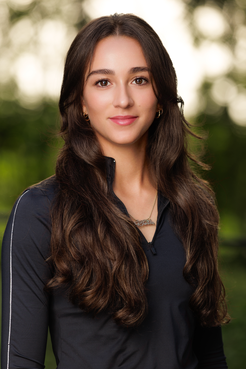 A woman with long hair is wearing a black shirt and a necklace.