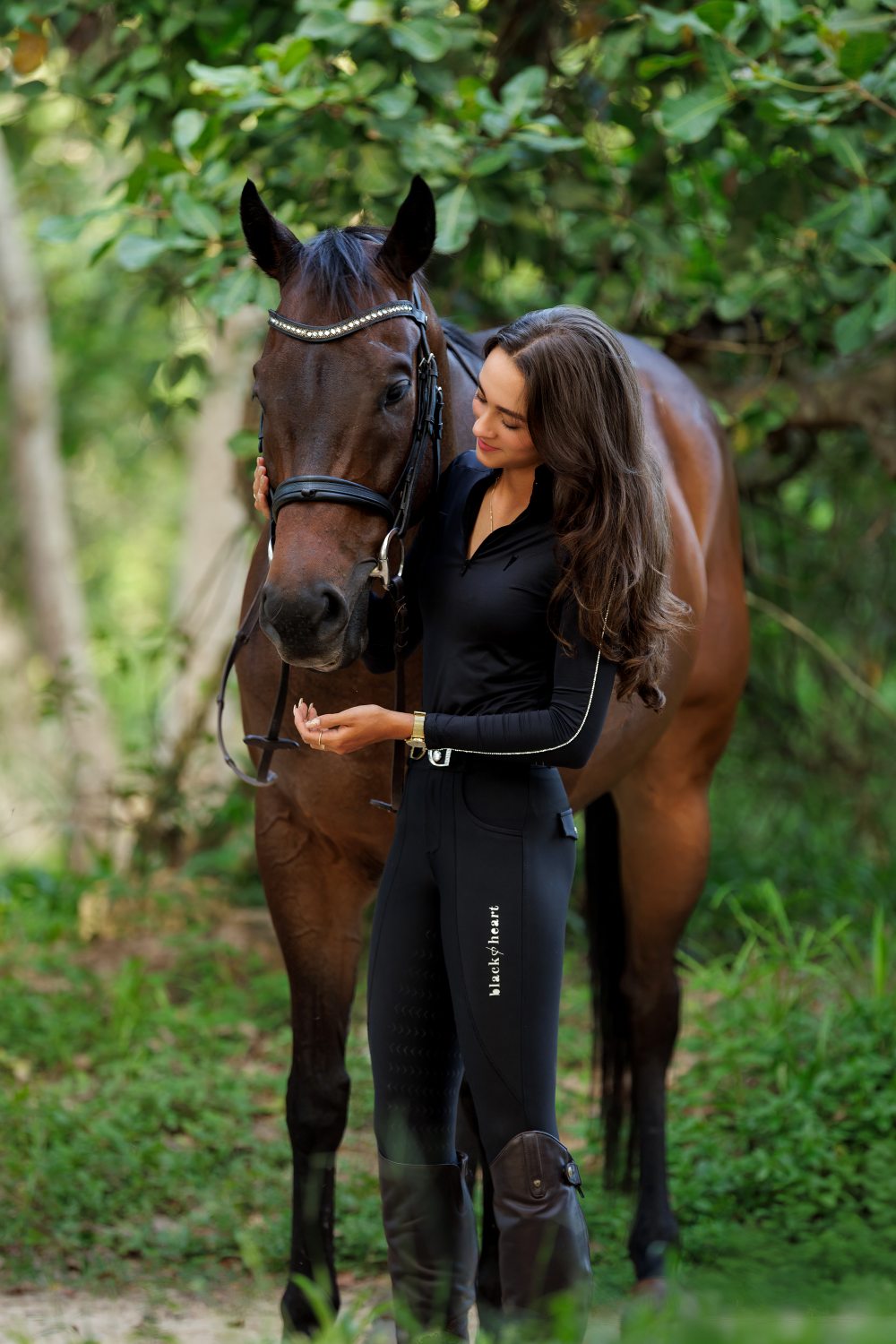 A woman is standing next to a brown horse in the woods.