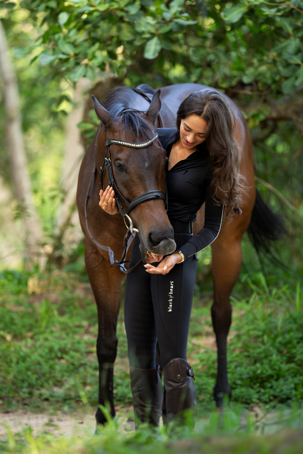 A woman is standing next to a brown horse in the woods.