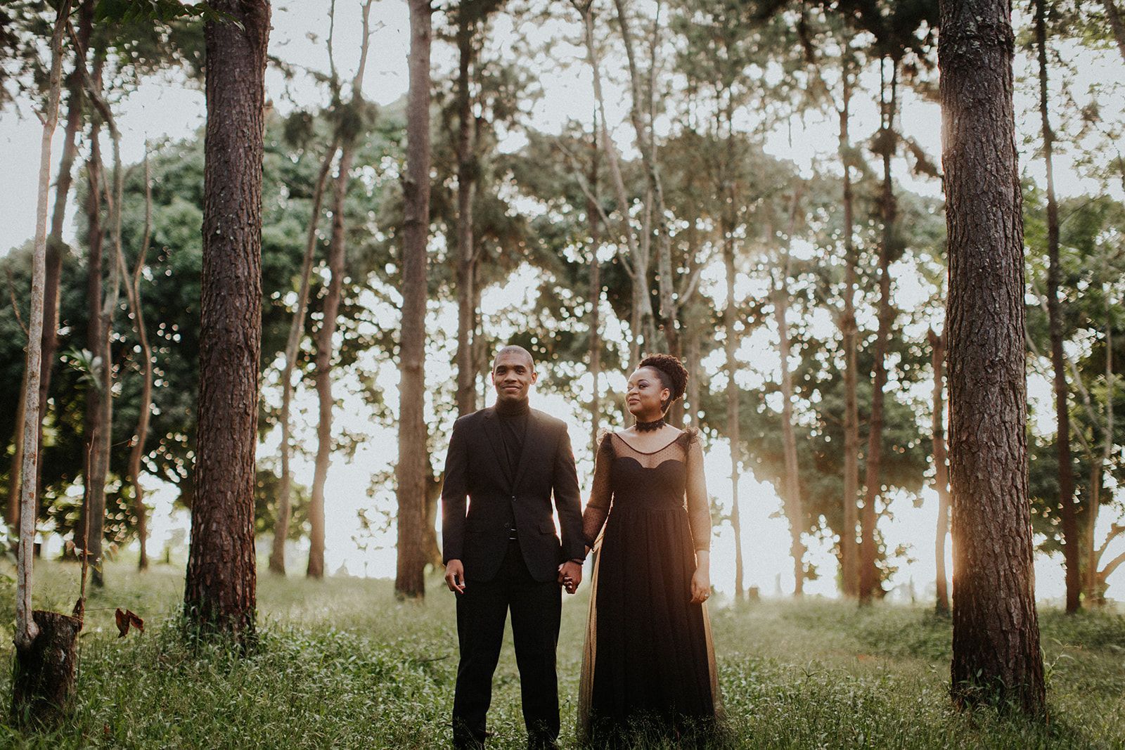 A man and a woman are standing in a forest holding hands.