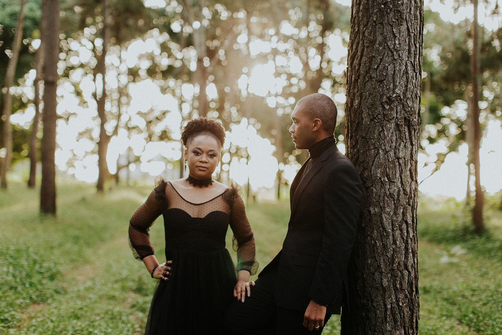 A man and a woman are leaning against a tree in the woods.