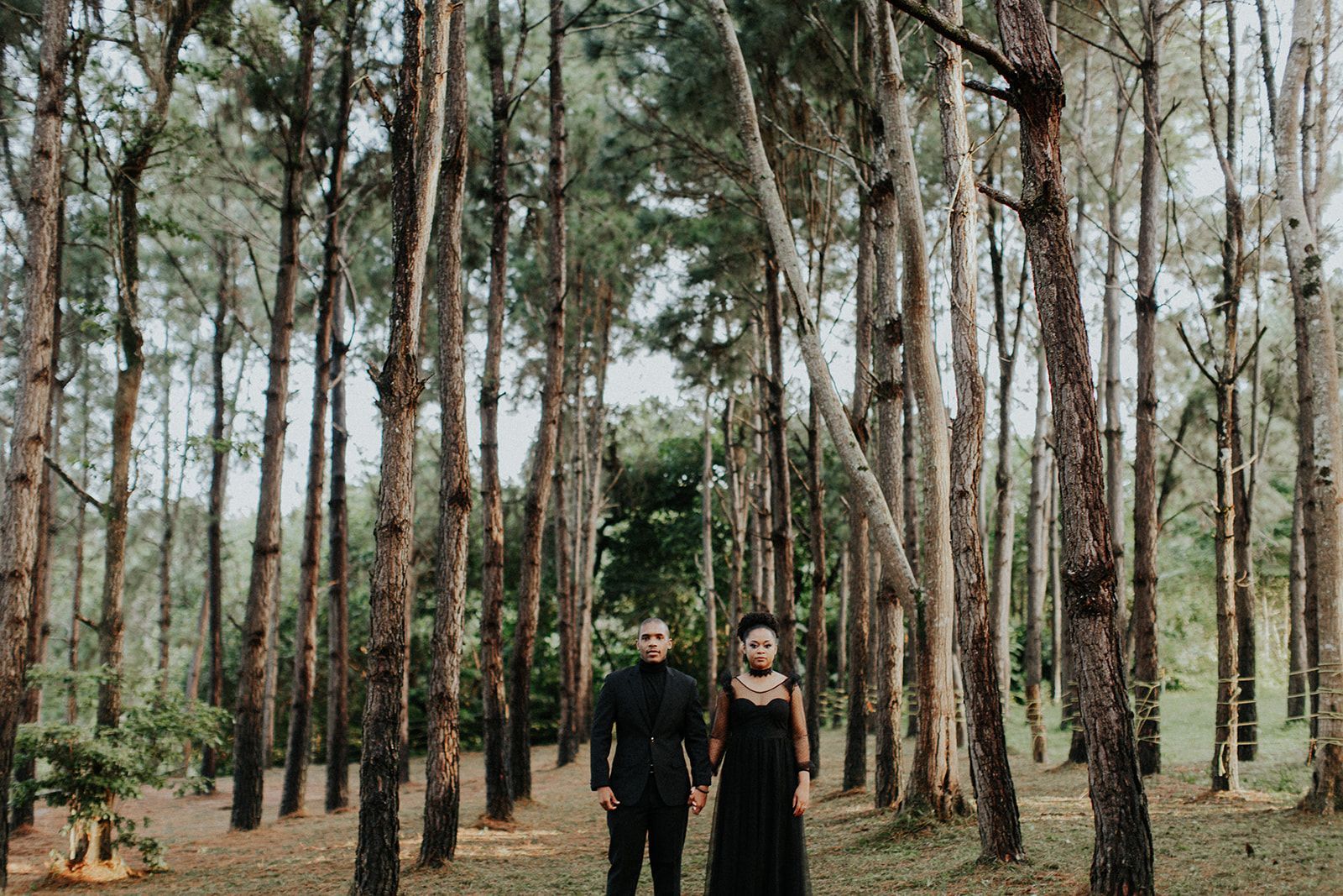 A man and a woman are standing in the middle of a forest.