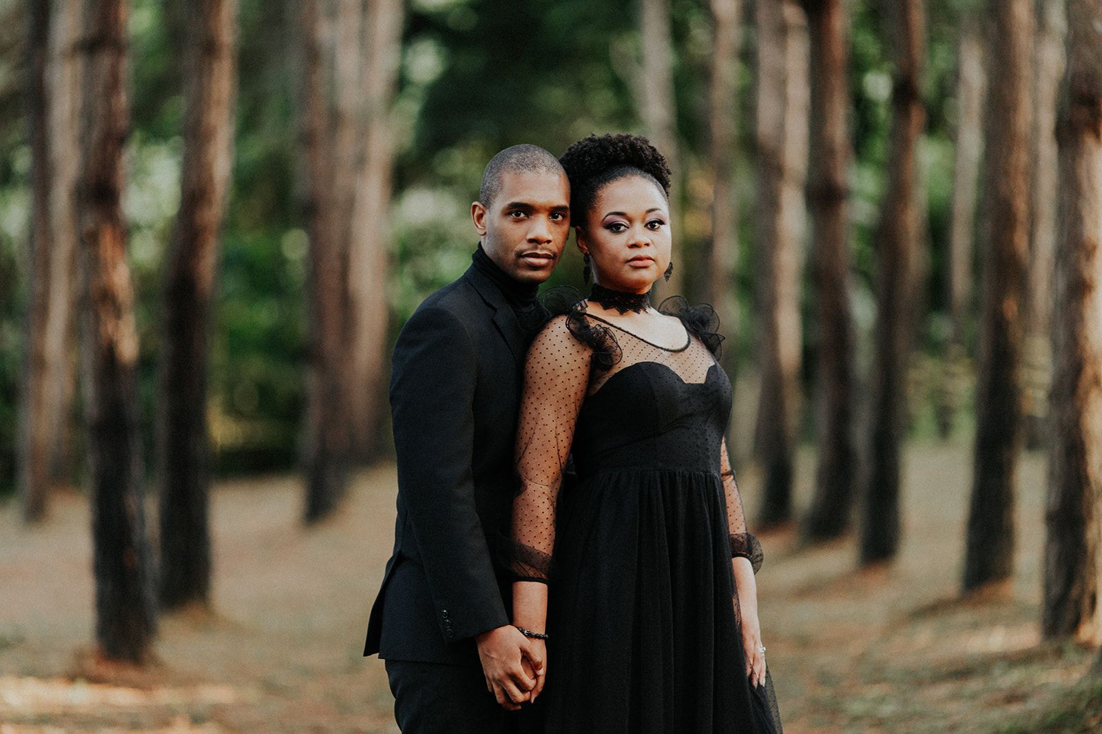 A man and a woman are standing next to each other in a forest holding hands.