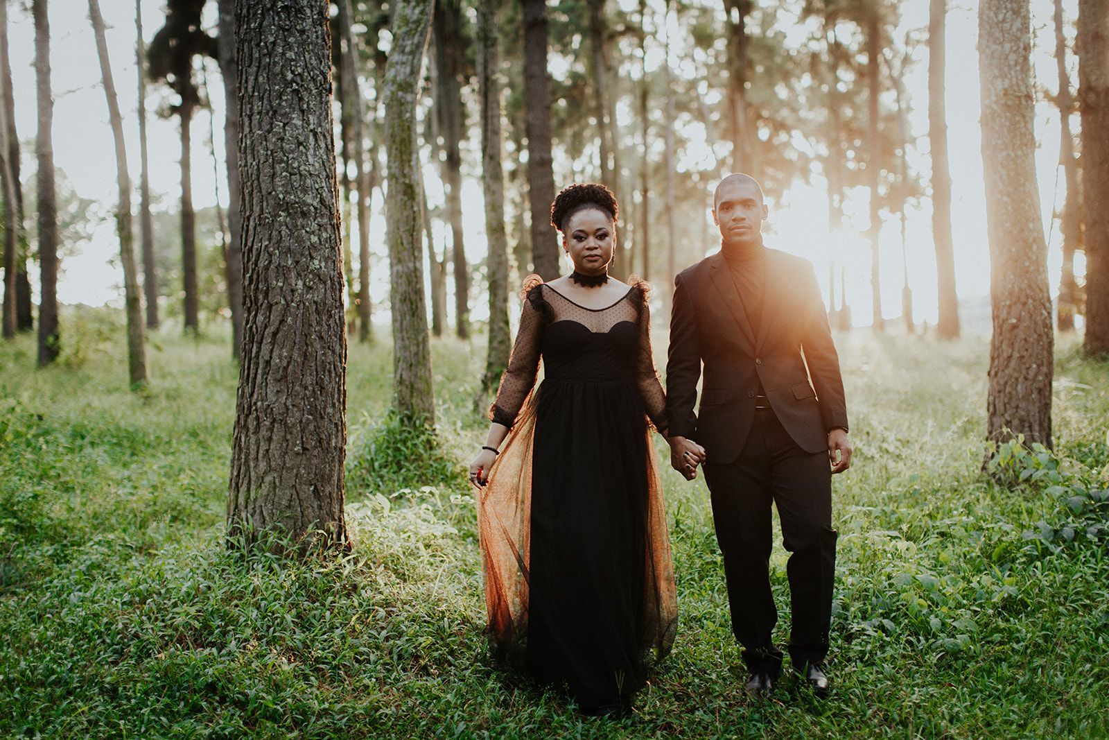 A man and a woman are walking through a forest holding hands.