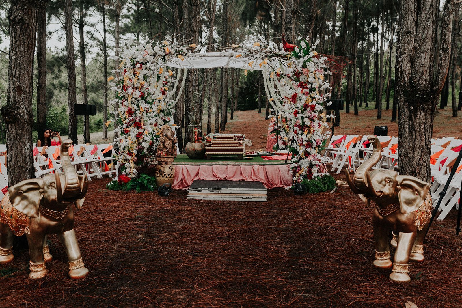 There are two elephant statues in front of a floral arch in the woods.