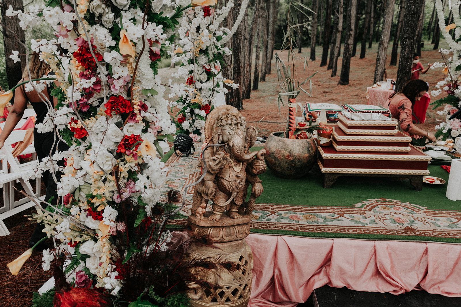 A statue of a deity is sitting on a table in front of a floral arrangement.