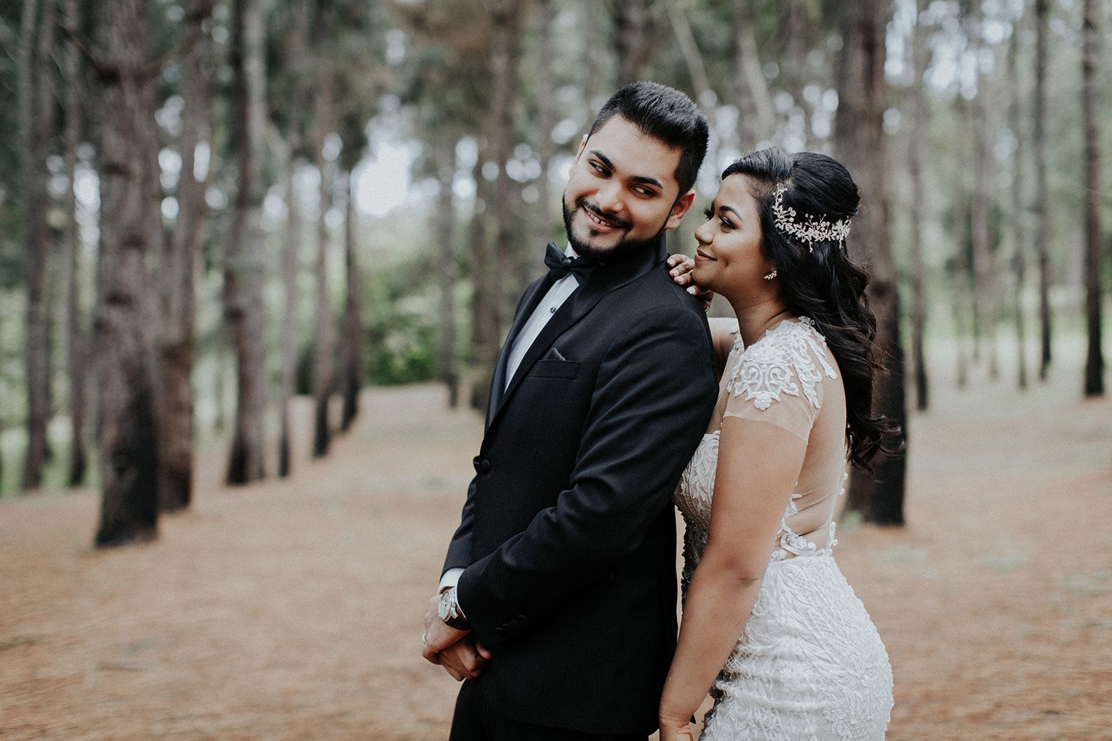 A bride and groom are posing for a picture in the woods.